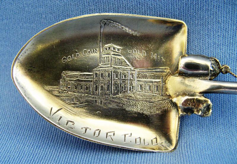 Souvenir Mining Spoon Bowl Gold Coin Mine Victor CO.JPG - SOUVENIR MINING SPOON GOLD COIN MINE VICTOR CO - Sterling silver souvenir spoon, gold washed bowl engraved with mining scene and buildings and marked GOLD COIN GOLD MINE VICTOR COLO, spoon in the form of a shovel and having a rope wrapped handle on which is affixed a pick, shovel, and moveable windlass crank at top and an ore bucket and nugget at bottom, back is marked Sterling, 5 3/4 inch long, 0.8 troy oz, ca. 1890s  [The Woods family, founders of Victor, Colorado, struck a rich vein of gold while excavating for the foundation of a hotel at 4th & Diamond Avenue in 1894. This vein became the Gold Coin Mine, one of the richest mines in the Cripple Creek District.  With this stroke of luck and fortune, the hotel was built at a new location.  Partners Charles L. Tutt, Spencer Penrose and Charles M. MacNeill purchased the Gold Coin Mine in the center of Victor in 1902 and renamed it the Granite Mine.  Remnants of the mine, as well as the Gold Coin Club built for the mine’s workers, have been preserved and can still be seen in Victor. The old Victor Hotel burned in the big fire of 1899, when Victor’s entire business district was leveled in one August afternoon.]